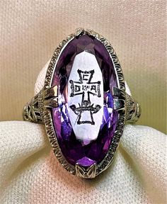 "Beautiful c1920 14k white gold ring with a filigree design, prong set with a faceted oval amethyst gemstone. The amethyst stone has a cross etched on the table of the stone with \"C D of A\" (Catholic Daughters of America) etched in it. The stone measures .8\" by .4\". It is a size 4.75 and can certainly be sized by a jeweler. It is unmarked by acid tests as 14k gold. This really is an unusual piece and beautifully done. The overall condition is considered to be extremely good and appears to ha Victorian Oval Engraved White Gold Ring, Oval Amethyst Jewelry Collectible, Art Deco Oval Amethyst Ring, Antique Oval Amethyst Ring, Antique Oval Purple Amethyst Ring, Oval Amethyst Collectible Ring, Art Deco Oval Purple Amethyst Ring, Antique Oval Purple Jewelry, Oval White Gold Engraved Collectible Ring