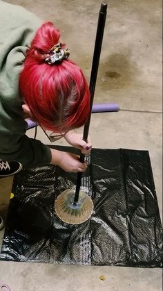 a woman with red hair is painting a piece of art on the ground while holding a paintbrush