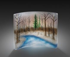 an artistic glass sculpture depicting a winter scene with trees and a pond in the foreground