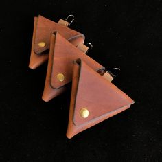 three triangle shaped leather keychains with brass hardwares on black background, closeup