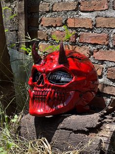 a red skull mask with horns on it sitting in front of a brick wall and grass