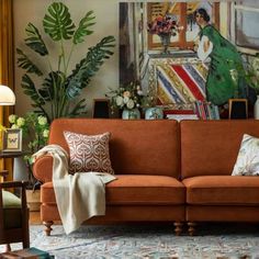 a living room with an orange couch and paintings on the wall behind it in front of a window