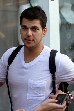 a man in white shirt and black backpack holding cellphone next to another man with shoulder bag