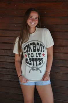 Saddle up and showcase your western pride with our Cowboys Do It Better Graphic Tee, a statement piece that combines style with a touch of cowboy charm. Crafted from soft and breathable cotton fabric, this tee offers all-day comfort whether you're wrangling cattle or just kicking back with friends. Featuring a bold and playful "Cowboys Do It Better" graphic print on the front, this tee is sure to turn heads and spark conversations wherever you go. The classic crew neckline and short sleeves make it perfect for casual wear, while the relaxed fit ensures a comfortable and flattering silhouette. Whether you're hitting the rodeo, hanging out at the local saloon, or simply running errands around town, this graphic tee is the perfect choice for showcasing your love for all things western. Pair i White Western T-shirt For Rodeo, White Short Sleeve Tops For Country Events, Western White T-shirt For Country Events, Western Style White T-shirt For Country Events, Western Crew Neck Tops For Country Events, Relaxed Fit Western T-shirt For Ranch, Western Style Relaxed Fit T-shirt For Ranch, White Crew Neck Tops For Western-themed Events, White Western Tops For Country Events