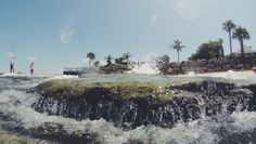 a man standing on top of a rock in the ocean next to a small waterfall