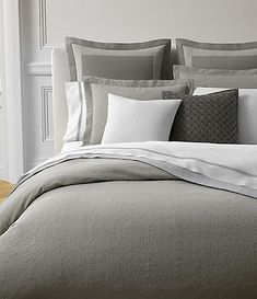 a bed with grey and white sheets and pillows