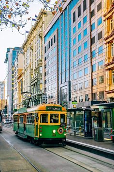 a green and yellow trolley is going down the street in front of some tall buildings