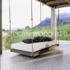 a bed sitting on top of a wooden platform next to a lush green field with mountains in the background