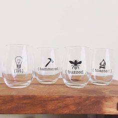 four wine glasses with different logos on them sitting on a wooden shelf next to a white wall