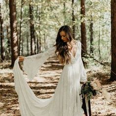 a woman in a white wedding dress holding her long flowing veil over her shoulder and looking down at the ground