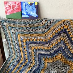 a crocheted blanket sitting on top of a wooden chair next to a painting