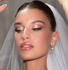 a woman wearing a wedding veil and holding her hand up to the side of her head