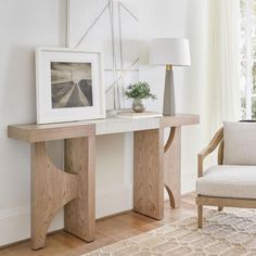 a wooden table with a white vase on it next to a chair and framed photograph