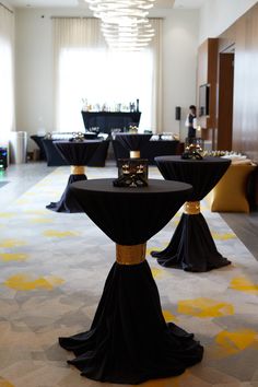 tables with black tablecloths and gold accents in a hotel lobby setting for an event