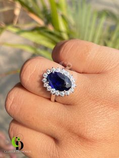 a woman's hand holding a ring with a blue stone and diamond halo around it