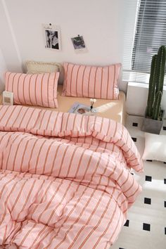 a bed with pink and white striped sheets in a small room next to a cactus