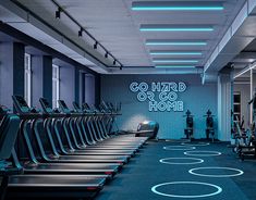 a gym with rows of treadmills and neon lights on the wall behind them