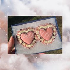 two pink heart shaped brooches in a blue box with clouds and stars around them