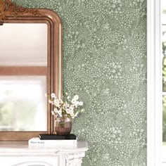 a mirror and vase with flowers in front of a wallpapered room that looks like it has been painted