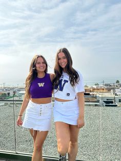 two young women standing next to each other on top of a roof with the ocean in the background