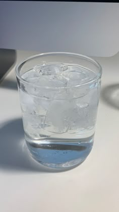 a glass filled with water sitting on top of a white table next to a computer mouse