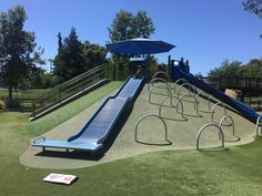 a blue slide in the middle of a playground with lots of chairs and umbrellas