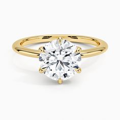 a yellow gold engagement ring with a round cut diamond in the center, on a white background