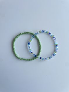 two bracelets sitting next to each other on top of a white surface with blue and green beads