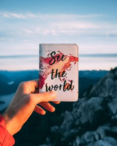 someone holding up a card with the words see the world on it in front of mountains