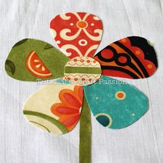 a close up of a flower made out of fabric on a white table cloth with red, orange and blue flowers