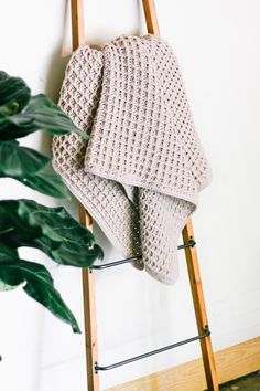 a crocheted blanket is hanging on a ladder next to a potted plant