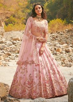 a woman in a pink lehenga standing on rocks