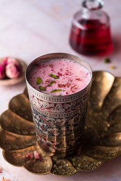 a cup filled with pink liquid sitting on top of a gold plate next to flowers