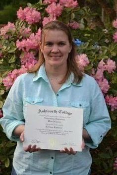 a woman is holding up a certificate in front of pink flowers and bushes with the caption