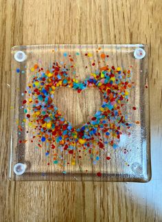 a heart made out of colorful sprinkles on a clear glass plate sitting on top of a wooden table