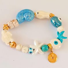 This beautiful elastic bracelet combines carefully selected porcelain and gold-tone steel charms, inspired by marine style 🌊. Each charm features delicate details like starfish, seashells, and evil eye beads, creating a unique and elegant accessory that complements any casual or beach look. Perfect for ocean and nature lovers! Handmade elastic bracelet with marine-themed porcelain charms Gold-tone steel accents for a touch of luxury ✨ Marine-inspired design with elements like seashells, turtles Porcelain Charms, Marine Theme, Handmade Porcelain, Eye Beads, Elastic Bracelet, Delicate Details, Elegant Accessories, Braided Bracelets, Starfish