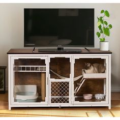 a cat sitting on top of a wooden cabinet in front of a flat screen tv