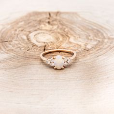 a white opal and diamond ring sitting on top of a tree stump