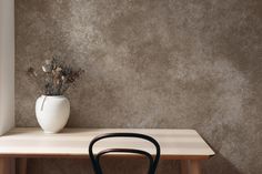 a white vase sitting on top of a wooden table next to a black metal chair