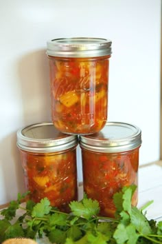 three jars filled with food sitting on top of a table next to cilantro