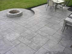 an outdoor patio with chairs, table and fire pit in the middle of grass area