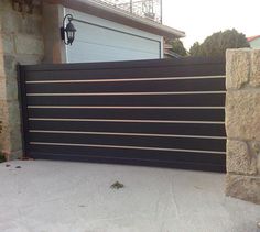 a black and silver gate in front of a stone building with a garage door behind it