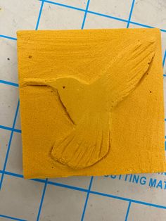 a yellow rubber stamp with a small bird on it's side and the words cutting mat below