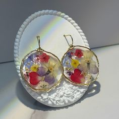 These resin colorful dried flower earrings are made from a variety of flowers, adding a touch of natural beauty to your look. Each earring features a delicate arrangement of dried flowers, preserved in a resin coating to maintain their vibrant colors and delicate textures. The resin also provides a protective layer, ensuring that the flowers will last for a long time. These earrings are perfect for those who appreciate the beauty of nature and want to add a touch of elegance to their everyday st Round Flower Earrings As A Summer Gift, Round Floral Print Jewelry Gift, Floral Print Round Jewelry Gift, Floral Print Round Jewelry For Gifts, Round Floral Print Jewelry For Gift, Multicolor Floral Print Flower Earrings, Bohemian Style Resin Flower Earrings As Gift, Flower-shaped Floral Print Earrings For Gift, Floral Print Flower Earrings For Gift