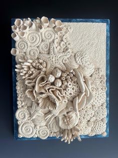 an intricately carved wall hanging with shells and seaweeds on the bottom, in white