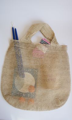 a jute bag with two pencils in it on a white table next to a blue and pink toothbrush