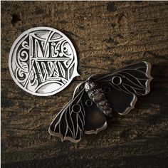 a silver and black moth sitting on top of a wooden table next to a round metal object