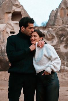 a man and woman standing next to each other in front of rock formations with their arms around each other