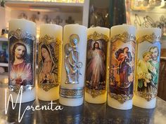 four candles with pictures of the virgin mary and jesus on them, all lined up in a row