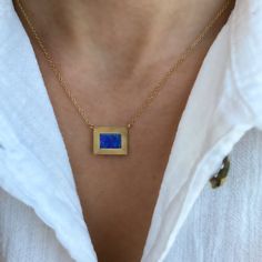 a woman wearing a necklace with a square shaped blue stone on it's gold chain